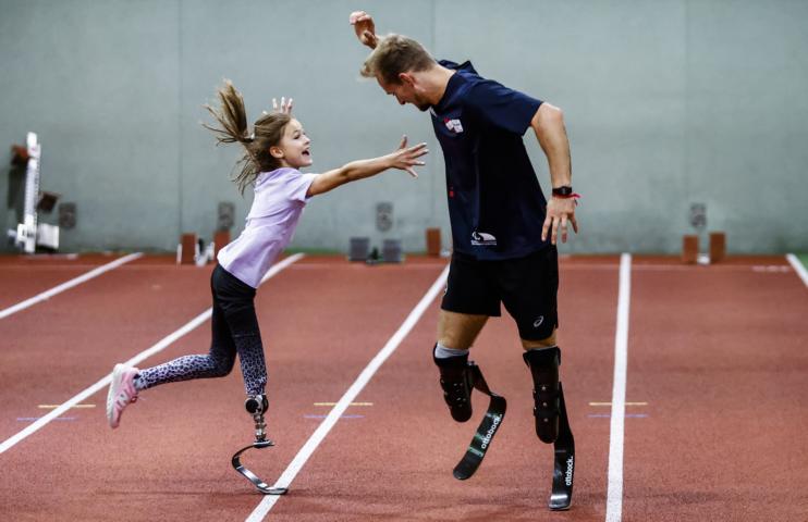 Johannes Floor und Kind beim Fangenspiel. Beide tragen Sportprothesen.